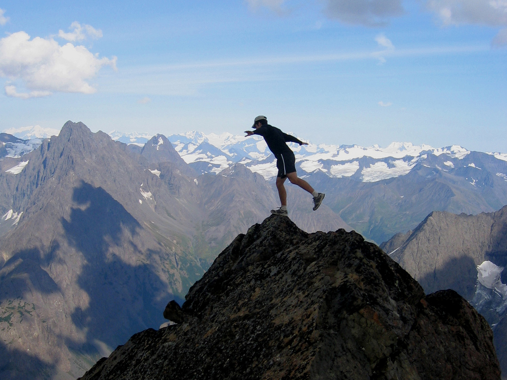 man balancing with one foot on a peak