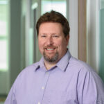 Headshot of Bill Swallow: White man with short brown hair and light beard wearing a purple shirt.