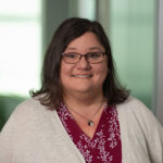 Headshot of Melissa Kershes: white female with brown glasses and shoulder-length brown hair, and a red shirt and light brown cardigan.