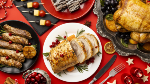 Red table cloth with a variety of savory holiday foods: chicken, turkey, cranberry, pork wellington,