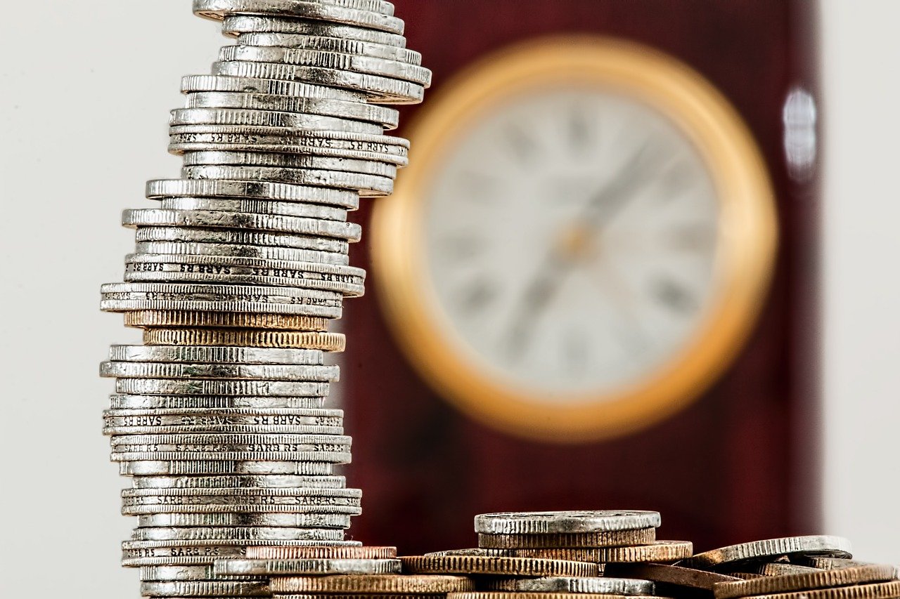 Stack of coins on the left with a blurred clock in the background.