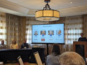 Photo of a panel of four people: seated from left to right, Jonathan Chandler (Intralox), Carrie Hane (Sanity), and Alan Pringle (Scriptorium). Standing, Marianne Calilhanna from DCL.