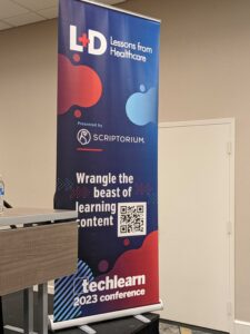 Image of a large red and blue stand-alone conference banner with the text "L+D lessons from Healthcare, Wrangle the Beast of Learning Content" with a QR code next to the text.