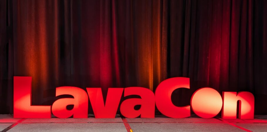 Grey stage and black curtains with large red letters standing up on stage that spell “LavaCon” and are lit up.