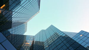 Photo of group of blue/glass skyscrapers taken from the bottom of the building with blue sky in between.