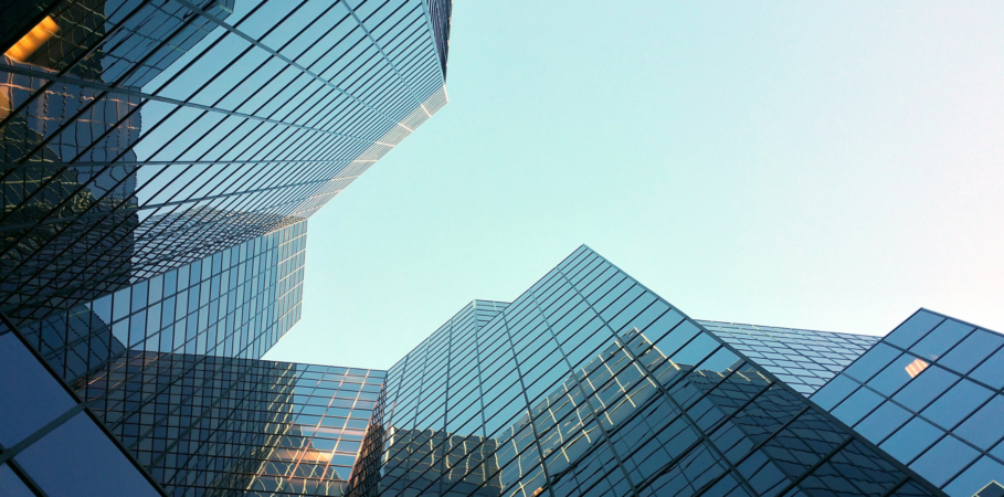 Photo of group of blue/glass skyscrapers taken from the bottom of the building with blue sky in between.