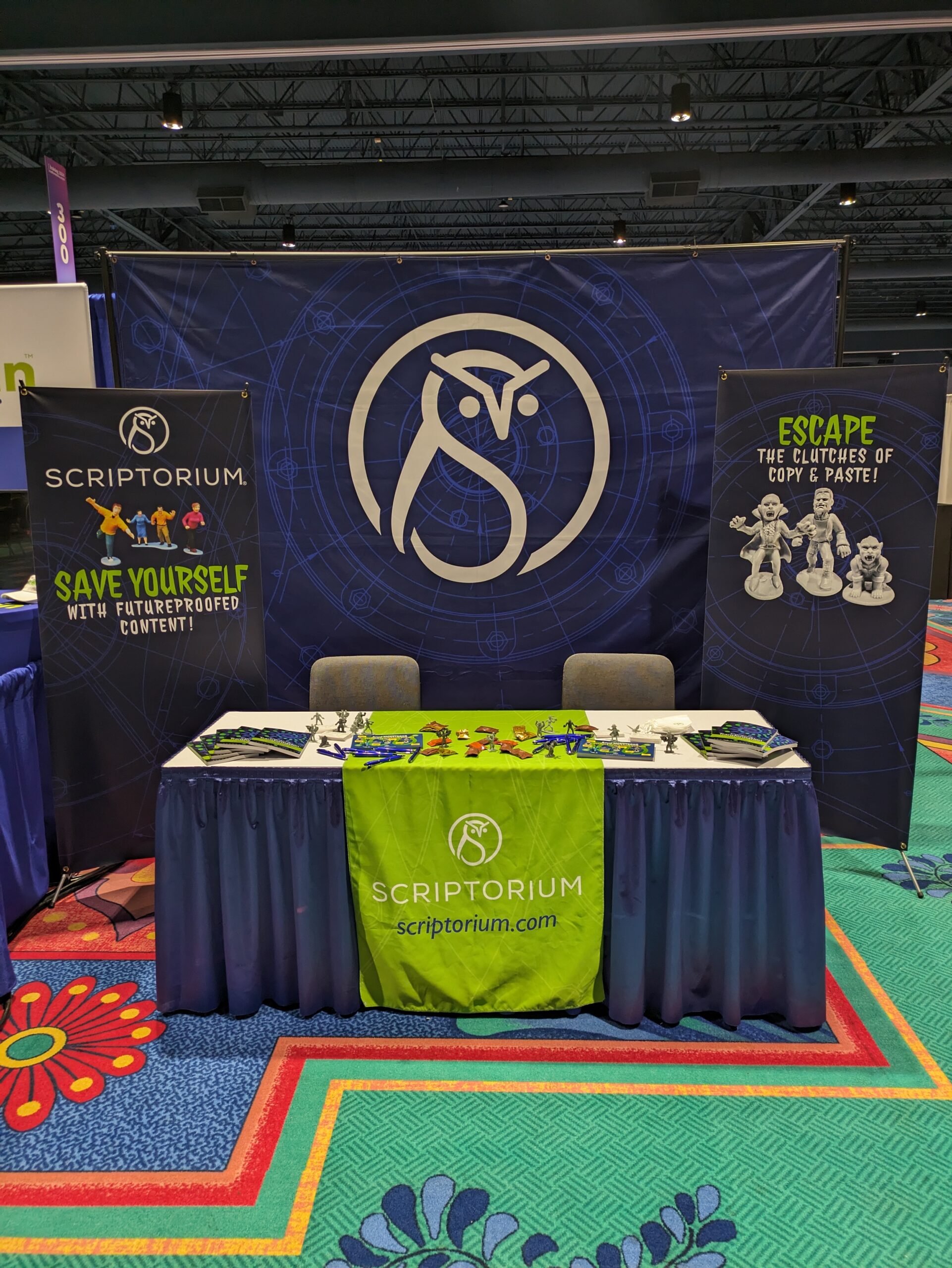 Picture of large booth set up at a conference expo floor with a blue background and and owl icon, blue banners, and a blue and white table with a bright green tablecloth.
