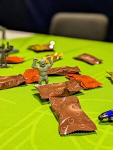 Green table with toy monster figure and individually wrapped chocolates. 