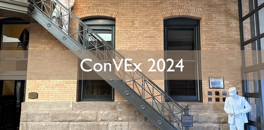 Interior brick wall with old-timey industrial staircase and paper-white mannequin figures of a policeman at the top of the staircase and a train conductor at the bottom. Transparent overlay box with white text says, "ConVEx 2024."